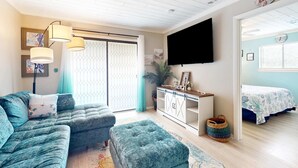 Una sala de estar con sofá, reposapiés y televisor montado en la pared.