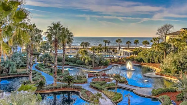 Un resort con varias piscinas, palmeras y vista al océano.