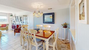 A dining area with a glass-top table, wooden chairs, a chandelier, and a framed mirror on the wall. - Coastal resort style villa with pool, golf, & balcony  WD, AC, & dog friendly (Hilton Head)