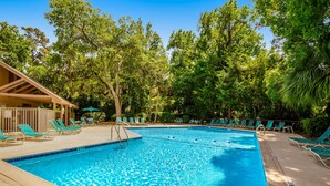 A swimming pool with lounge chairs, a wooden deck, and trees in the background. - Coastal resort style villa with pool, golf, & balcony  WD, AC, & dog friendly (Hilton Head)
