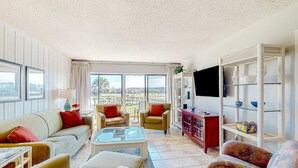 A spacious living room with a sofa, chairs, a coffee table, a TV, and a bookshelf. - Coastal resort style villa with pool, golf, & balcony  WD, AC, & dog friendly (Hilton Head)