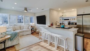 A modern kitchen with a central island, bar stools, a sofa, and a TV. - 3 bedroom home Palm lined hideaway with pool and Dog Friendly (Hilton Head)