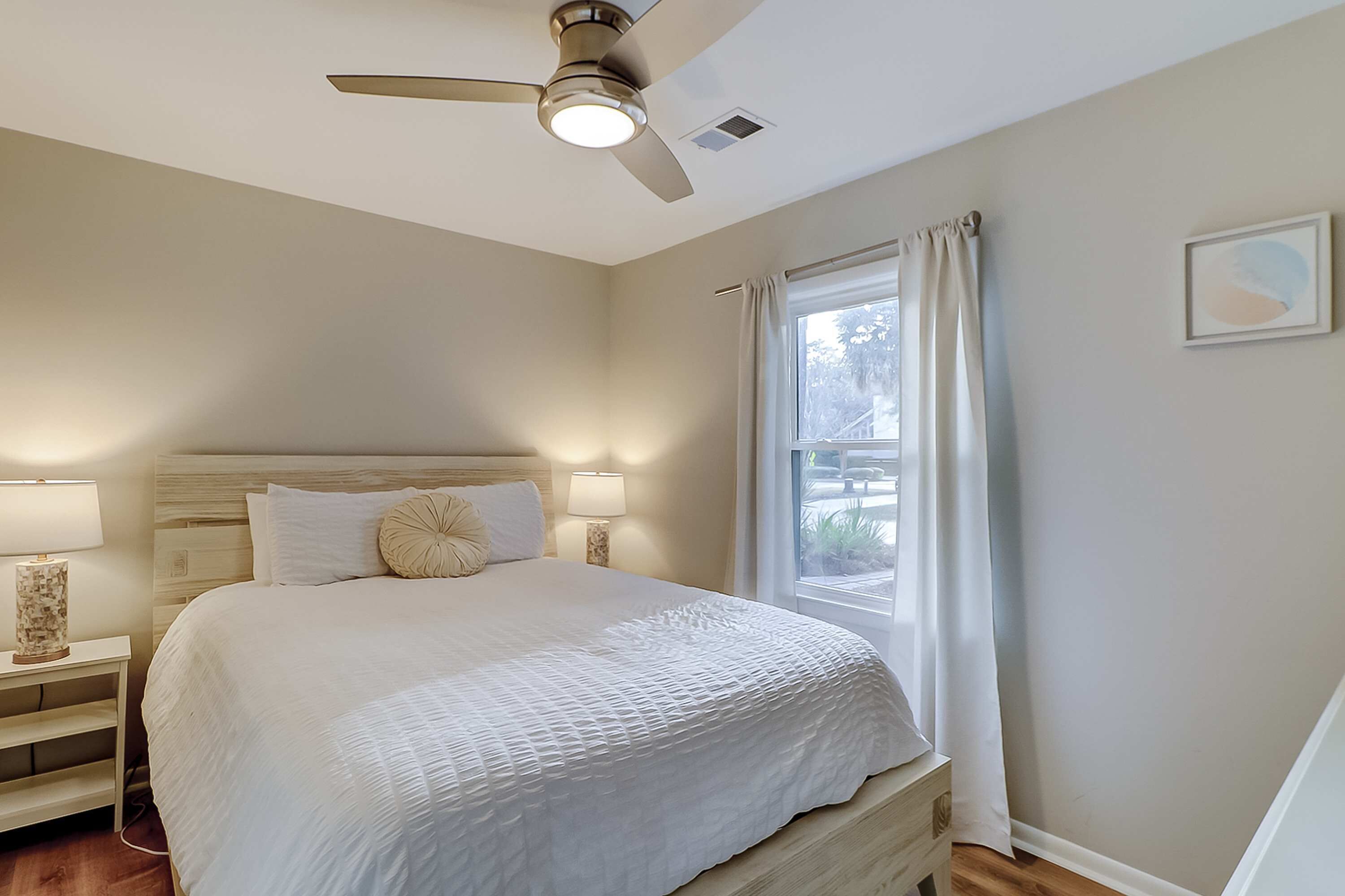 Ein Schlafzimmer mit Bett, Deckenventilator, Fenster mit Vorhängen und Nachttischlampe.