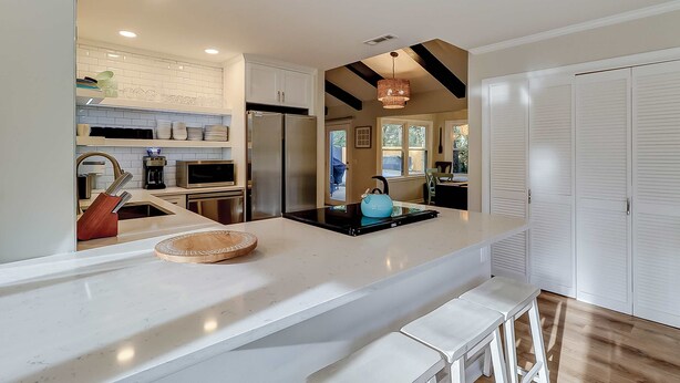 A modern kitchen with white cabinetry, a stainless steel refrigerator, a black induction cooktop, and a hanging light fixture. - 3 bedroom home Palm lined hideaway with pool and Dog Friendly (Hilton Head)