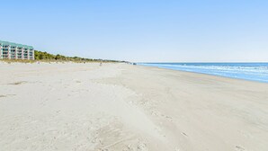 A beach with a hotel in the background, sandy beach, and ocean. - 3 bedroom home Palm lined hideaway with pool and Dog Friendly (Hilton Head)