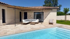Una casa moderna amb una piscina, un porxo cobert amb un sofà i butaques, i una finestra gran.