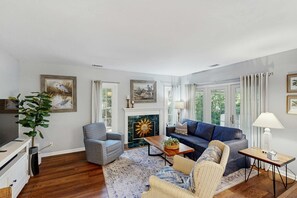 A living room with a fireplace, a sofa, a chair, a television, and a plant. - Renovated Dog Friendly Villa with Patio & Pool  Near Golf & Beach (Hilton Head)