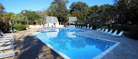 A rectangular swimming pool with a tiled deck, surrounded by lounge chairs and trees.