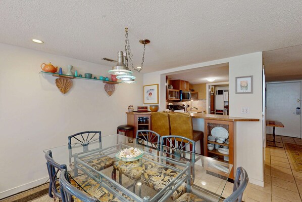 A dining area with a glass table, chairs, and a kitchen in the background. - Second-Floor Condo with WiFi, Pool, Golf Course Views - Near the Beach (Hilton Head)
