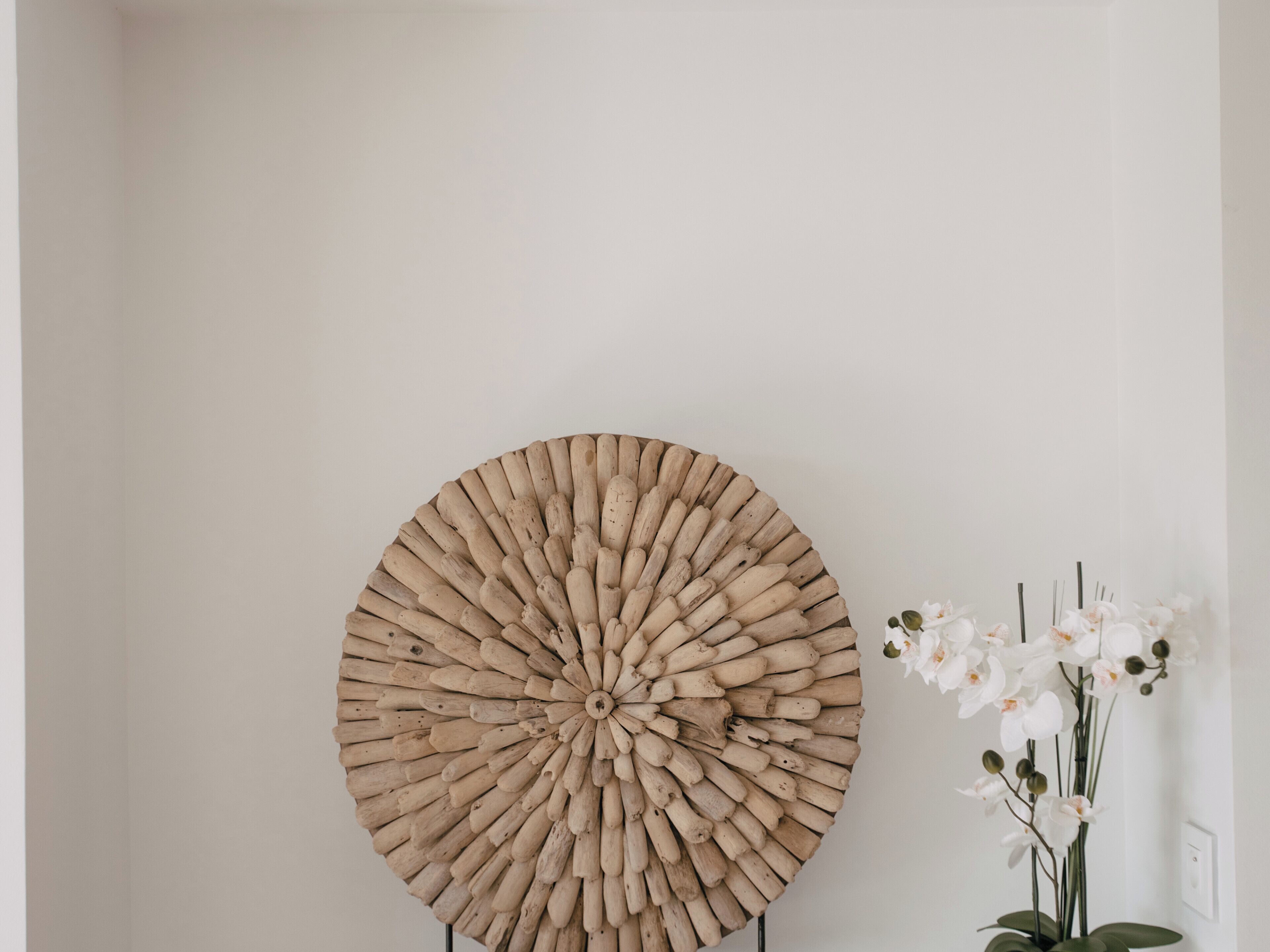 A circular wooden wall art piece and a vase with white flowers.