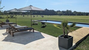 Un área junto a la piscina con sillones de descanso, una pérgola y vistas del paisaje circundante.
