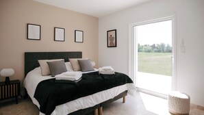 Un dormitorio con cama, mesitas de noche, ventana y cuadros en la pared.