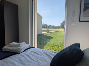 Un dormitorio con cama, ventana y vista a un área verde exterior.