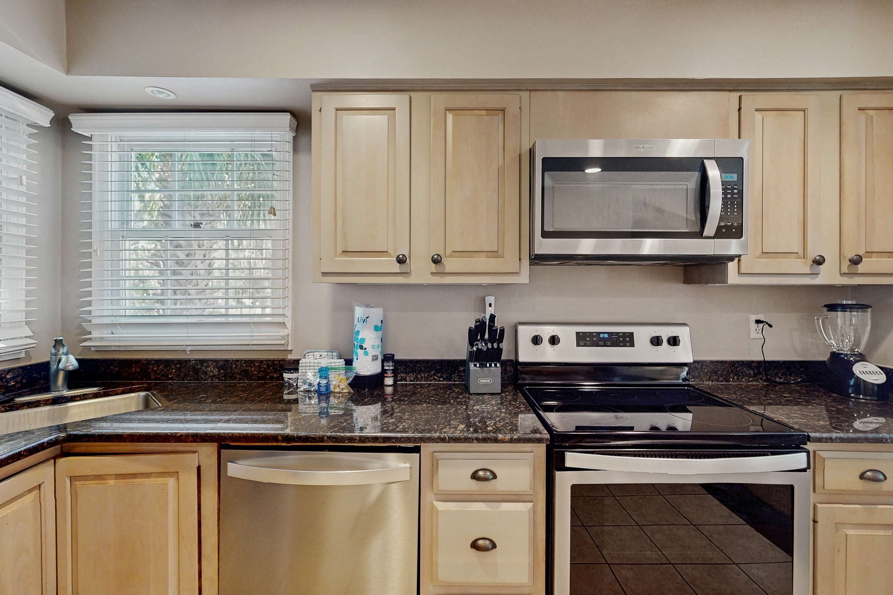 A kitchen with wooden cabinets, a microwave, stove, dishwasher, and a window with blinds.