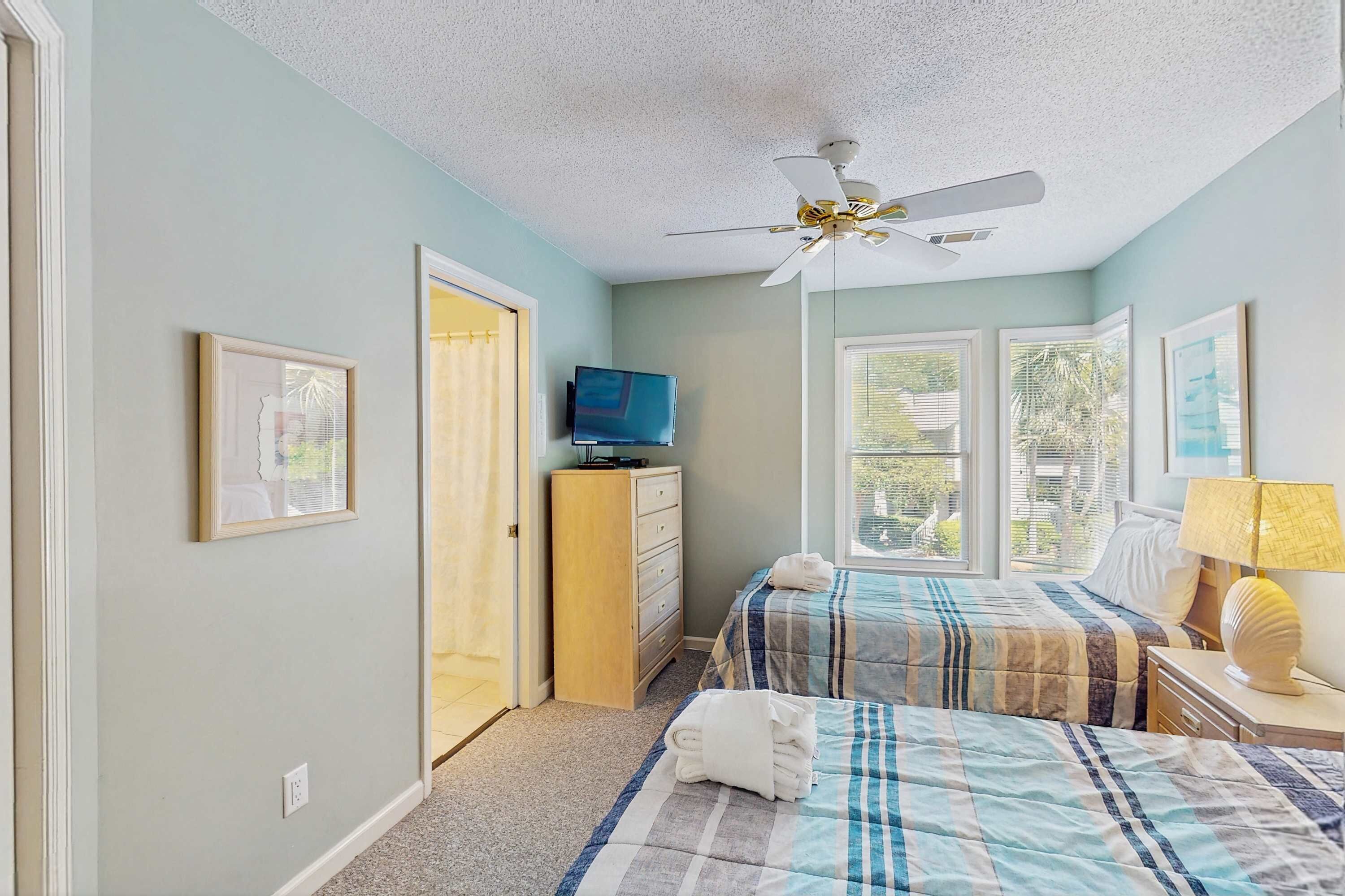 A bedroom with two beds, a ceiling fan, a TV, and a window with a view.