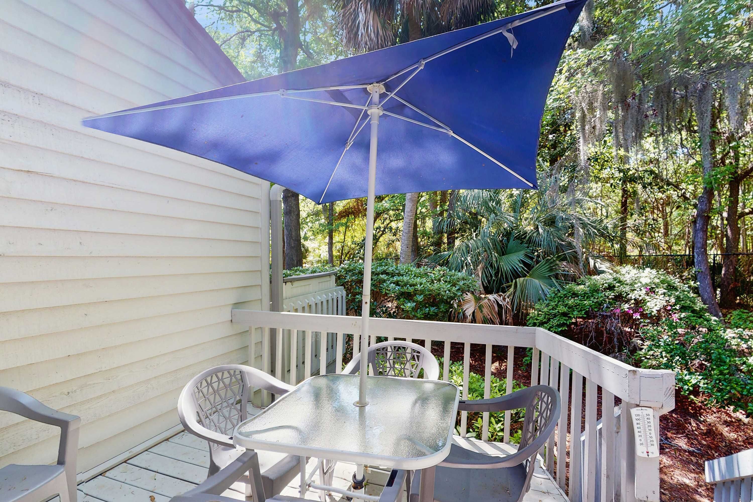 A covered patio with a table and chairs, surrounded by a white railing and lush greenery.