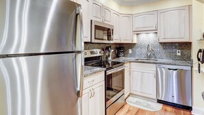 Cocina con electrodomésticos de acero inoxidable, encimeras de granito y armarios blancos.