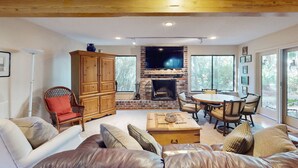 A living room with a fireplace, wooden furniture, and large windows. - Lovely house with gourmet kitchen, screened porch, & open deck (Hilton Head)