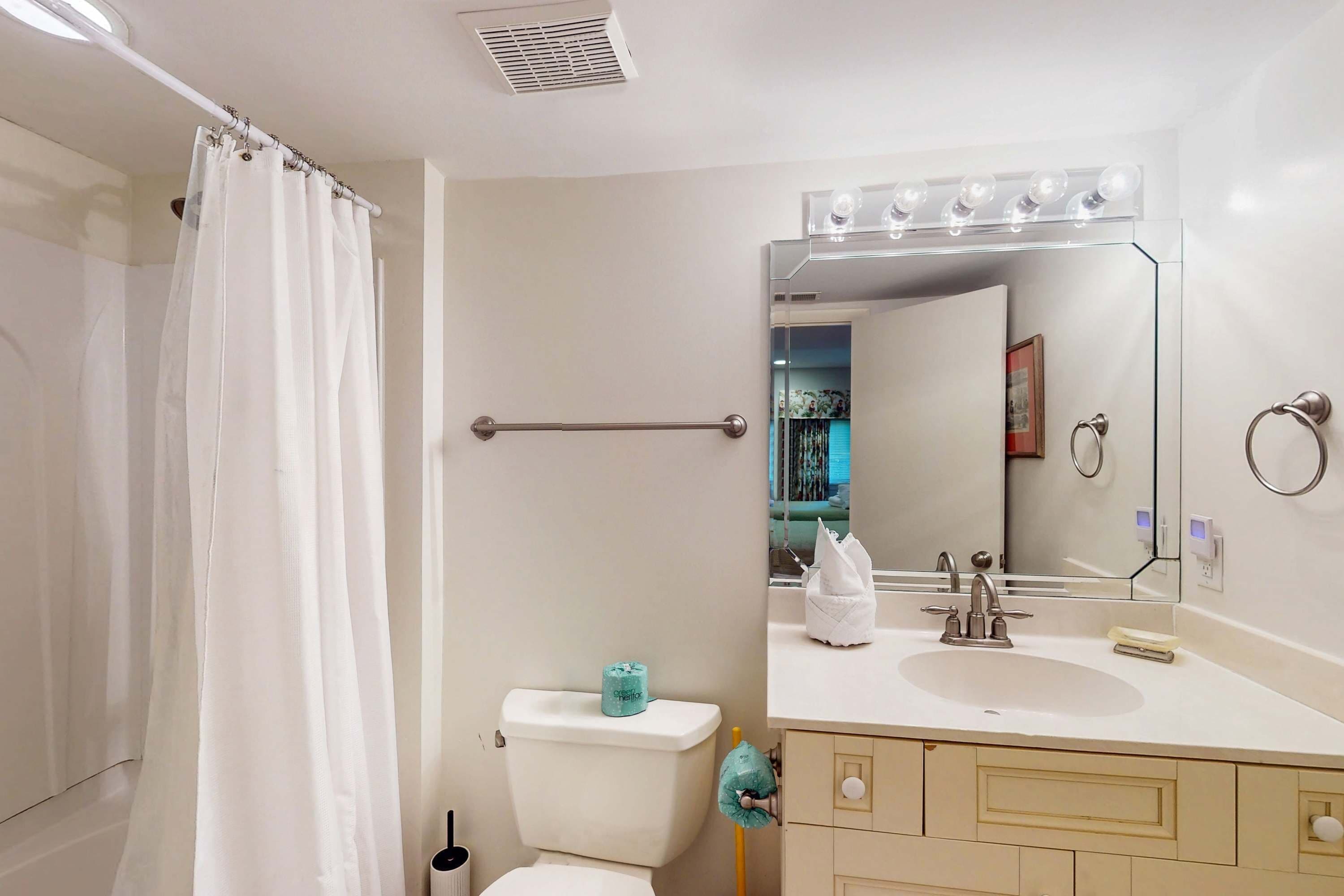 A bathroom with a shower curtain, a toilet, a sink with a mirror, and a towel rack.