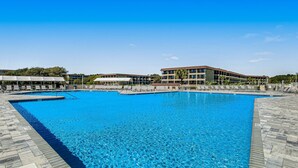 Ein großer Swimmingpool mit klarem, blauem Wasser, umgeben von einer gefliesten Liegefläche und einem Mehrstöckgebäude mit Balkonen.