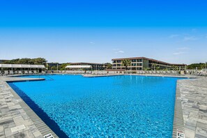 Ein großer Swimmingpool mit klarem, blauem Wasser, umgeben von einer gefliesten Liegefläche und einem Mehrstöckgebäude mit Balkonen.