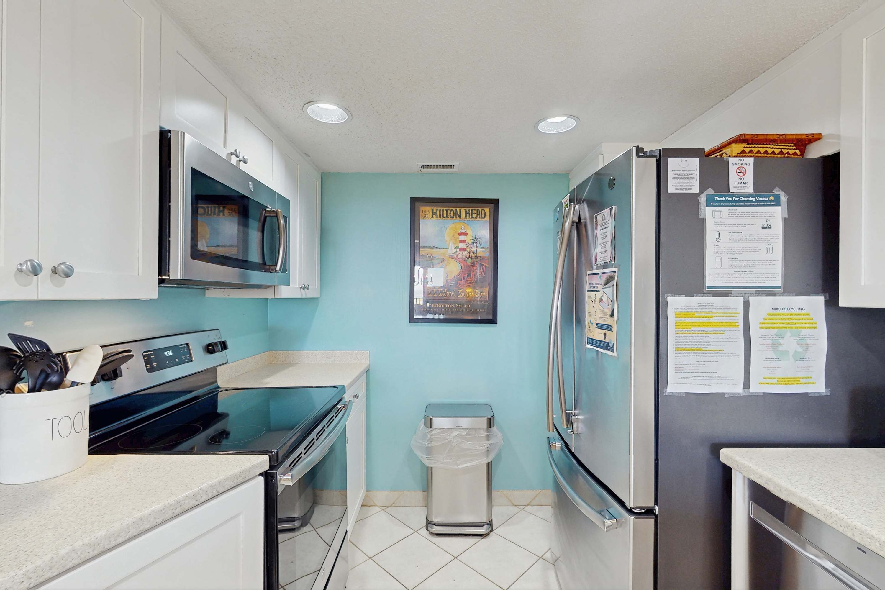 A kitchen with white cabinets, a stainless steel refrigerator, a microwave, and a trash bin.