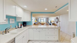A kitchen with white cabinets, a large island, and a dining area with wooden chairs and a chandelier. - Oceanfront Villa with Ocean Views, Shared Pool/Hot Tub, and Nearby Beach Access (Hilton Head)