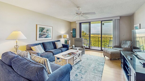 A living room with a sofa, armchair, coffee table, TV, and balcony with a view. - Oceanfront Villa with Ocean Views, Shared Pool/Hot Tub, and Nearby Beach Access (Hilton Head)