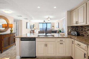 A kitchen with white cabinetry, a dishwasher, a granite countertop, and a view to the outside. - Quiet Waterfront Condo with WiFi - Pools & Hot Tub On-Site (Hilton Head)