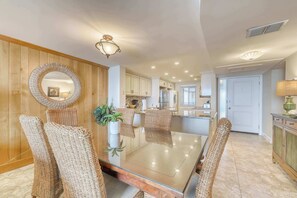 A dining area with a glass table, woven chairs, a round mirror, and wooden paneling. - Quiet Waterfront Condo with WiFi - Pools & Hot Tub On-Site (Hilton Head)