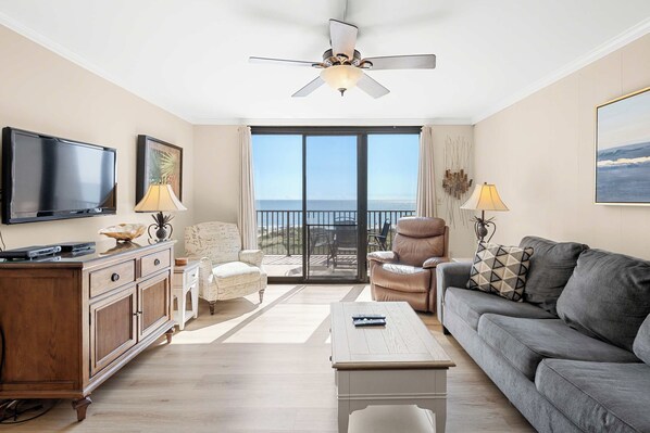 A living room with a television, a sofa, a coffee table, a chair, and a ceiling fan. - Quiet Waterfront Condo with WiFi - Pools & Hot Tub On-Site (Hilton Head)