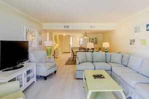 A living room with a TV, sofa, armchair, and coffee table. - Calming Condo Getaway with Shared Pool, Hot Tub, and Tennis Courts (Hilton Head)
