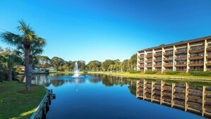 Un hotel con un estanque reflectante, una fuente y una palmera.