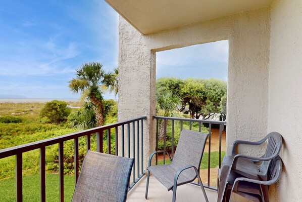 A balcony with two chairs, a railing, and a view of a green landscape. - Serene Oceanfront Villa with WiFi, Pool, Hot Tub, & Fitness Center (Hilton Head)