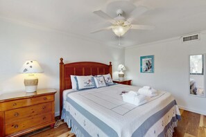 A bedroom with a wooden bed, a ceiling fan, a nightstand with a lamp, a dresser, and a framed picture on the wall. - Serene Oceanfront Villa with WiFi, Pool, Hot Tub, & Fitness Center (Hilton Head)