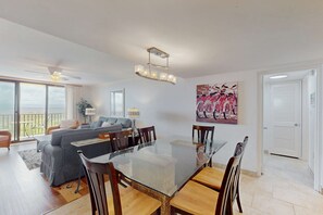 A modern living room with a glass-top dining table, a sofa, and a ceiling fan. - Serene Oceanfront Villa with WiFi, Pool, Hot Tub, & Fitness Center (Hilton Head)