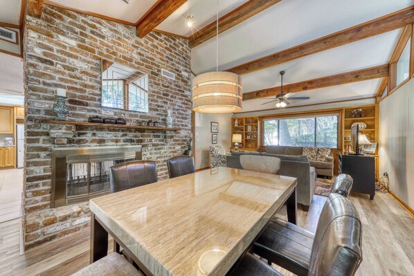 A spacious living area with a stone fireplace, a large dining table, and a cozy seating arrangement. - Pet Friendly Beach Getaway with Private Pool & Big Backyard Easy Walk to Beach (Hilton Head)