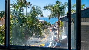 A coastal street with palm trees, a clear blue sky, and a view of the ocean. - Coastal Condo Steps to Beach & Downtown (San Clemente)