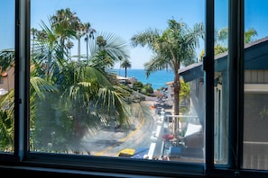 A coastal street with palm trees, a clear blue sky, and a view of the ocean.