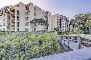A multi-story residential building with balconies, a wooden deck, and landscaped greenery. - Elegant Condo with Pool & Hot Tub, Lagoon View & Private Patio (Hilton Head)