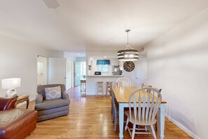 Una sala de estar con sofá, una mesa de comedor con sillas, una zona de cocina con taburetes y un reloj en la pared.