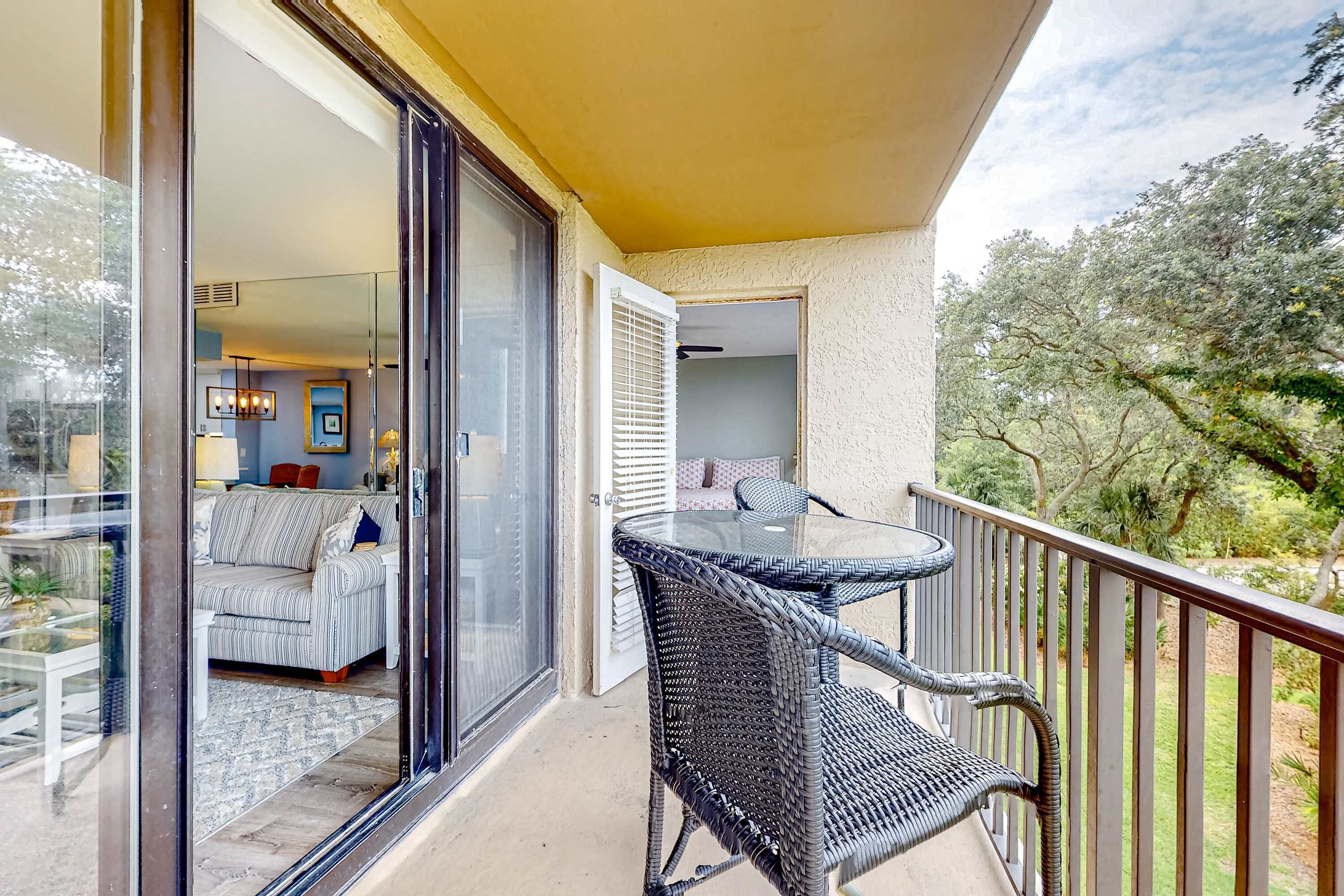Un balcon doté d’une porte vitrée donnant sur un espace de vie, ainsi que d’une table et de chaises en osier.