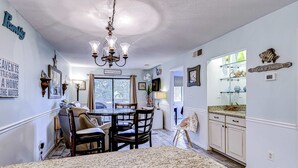 A dining area with a chandelier, a table with chairs, a kitchen with cabinets, and a window with a view. - Updated island Villa with two pools, tennis, & game room - walk to the beach (Hilton Head)