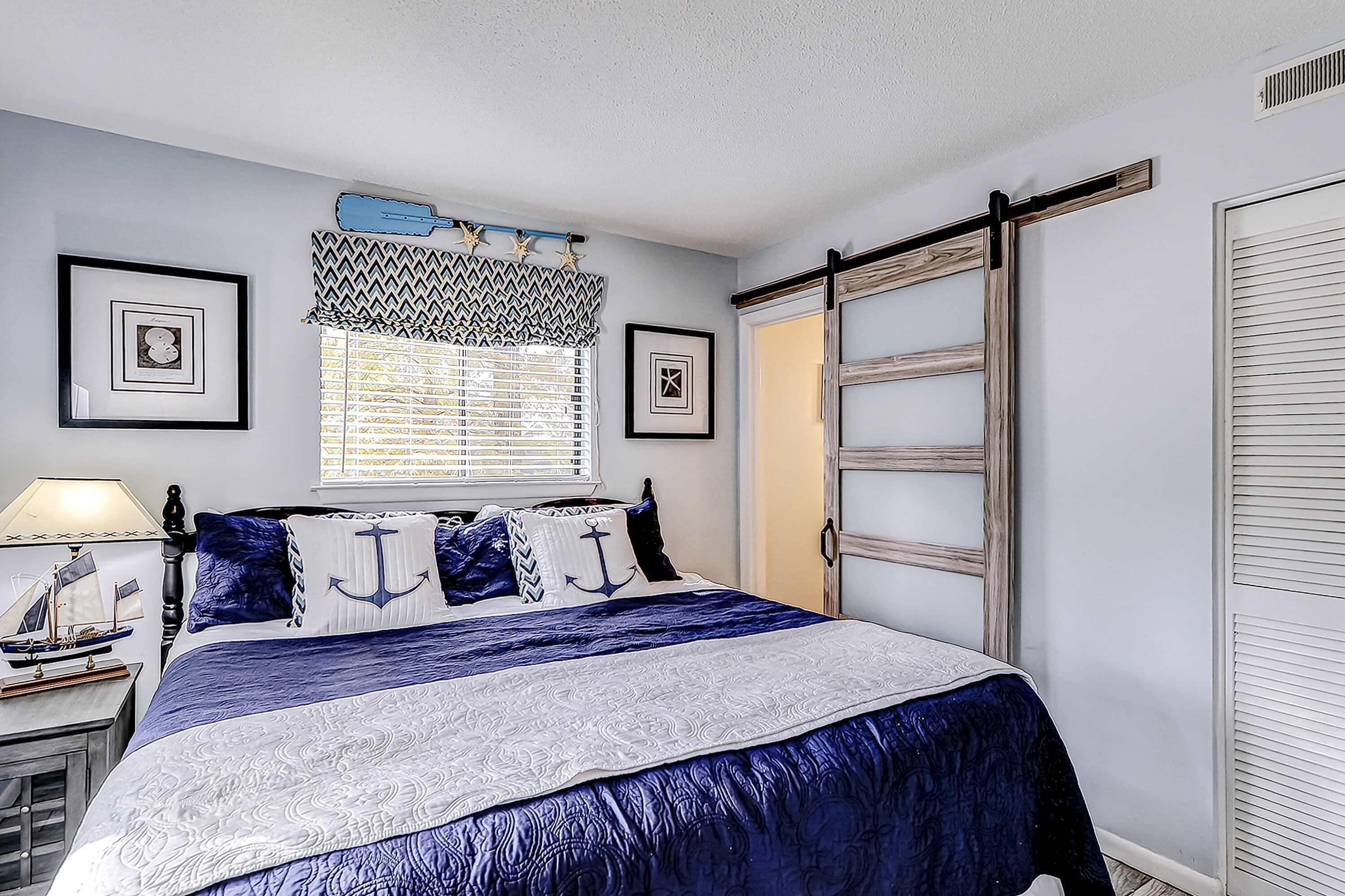 Un dormitorio con una cama, una ventana con persianas, una lámpara y cuadros enmarcados en la pared.