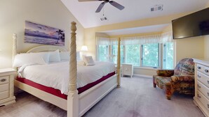 Ein Schlafzimmer mit einem Himmelbett, einem Deckenventilator, einem Fernseher, einem Sessel und einem Fenster mit Jalousien.