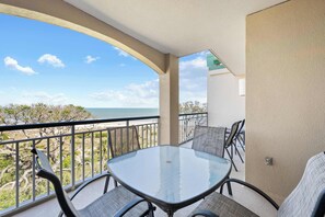 A balcony with a glass table and chairs, overlooking a beach and ocean. - Stunning beach condo with two ocean-view balconies, shared pool & hot tub (Hilton Head)