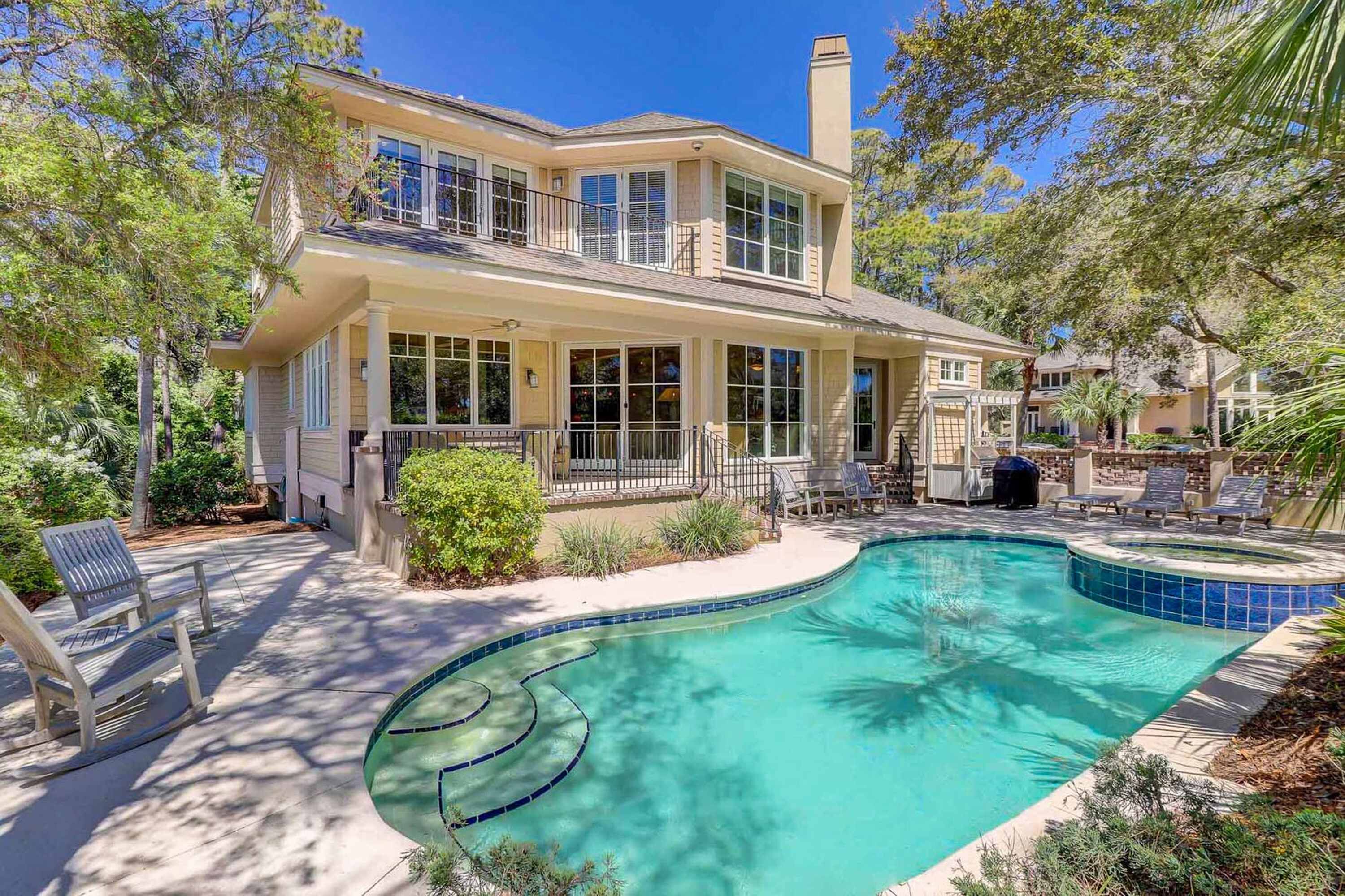 A two-story house with a swimming pool, outdoor seating, and a covered patio area.