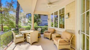 A covered outdoor seating area with wicker furniture, a ceiling fan, and a view of surrounding greenery. - Two-story home with pool, balcony, deck, grill, & central AC - snowbirds welcome (Hilton Head)