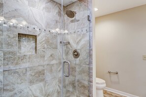 Un baño con ducha de vidrio, inodoro y piso de baldosas.