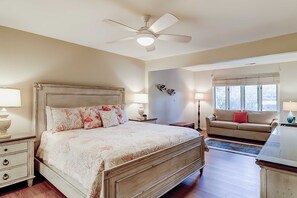 Un dormitorio con cama, mesitas de noche, ventilador de techo, ventana y un sofá.